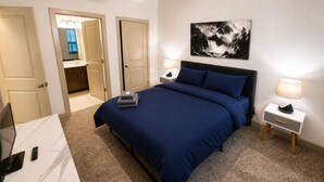 A hotel room with a bed, bedside tables, a desk with a laptop, and a painting on the wall. - Iron City Retreat | Modern 2BR Stay #4 (Birmingham)