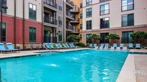 A swimming pool with lounge chairs, surrounded by multi-story buildings with balconies. - Iron City Retreat | Modern 2BR Stay #4 (Birmingham)