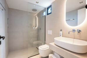 A modern bathroom with a glass-enclosed shower, a white sink, and a large mirror. - Maessa Suites (Lukove)