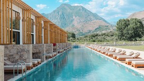 A pool with lounge chairs, a stone wall, and a mountain view. - Maessa Suites (Lukove)