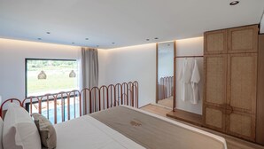 A modern bedroom with a large bed, a view of a garden, a wooden wardrobe, and a balcony with a railing. - Maessa Suites (Lukove)