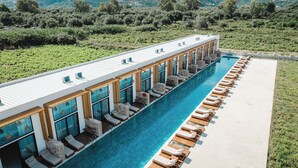 A modern hotel with a long pool, outdoor seating, and a view of the surrounding greenery. - Maessa Suites (Lukove)