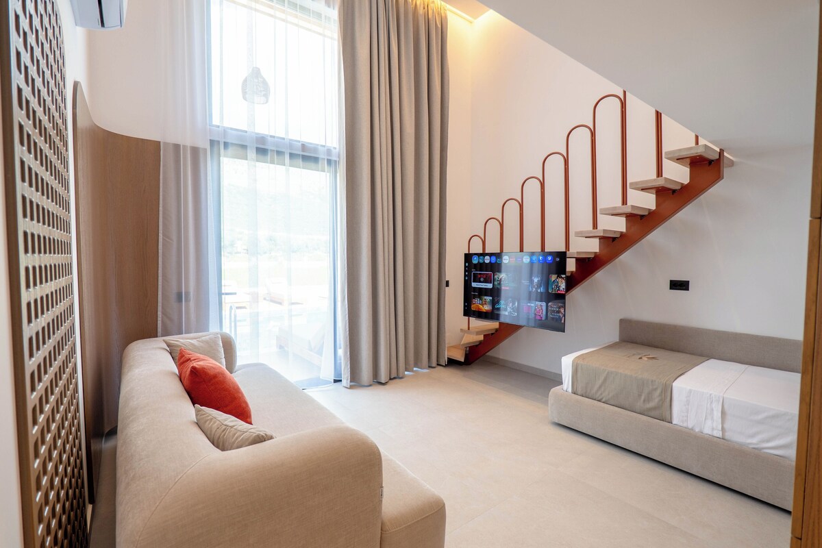 A modern living room with a sofa, a television, and a staircase.