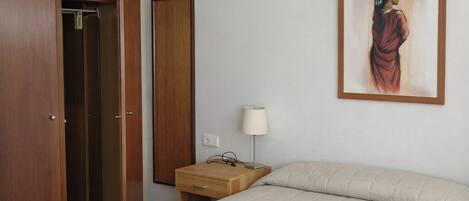 A bedroom with a bed, a wardrobe, a nightstand, a lamp, and a framed picture on the wall.