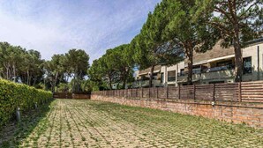 A paved courtyard with a brick wall, trees, and a building with multiple windows. - Duplex apartment 800 meters from the beach, in a high-end residential complex, in a quiet area (Castell d'Aro)
