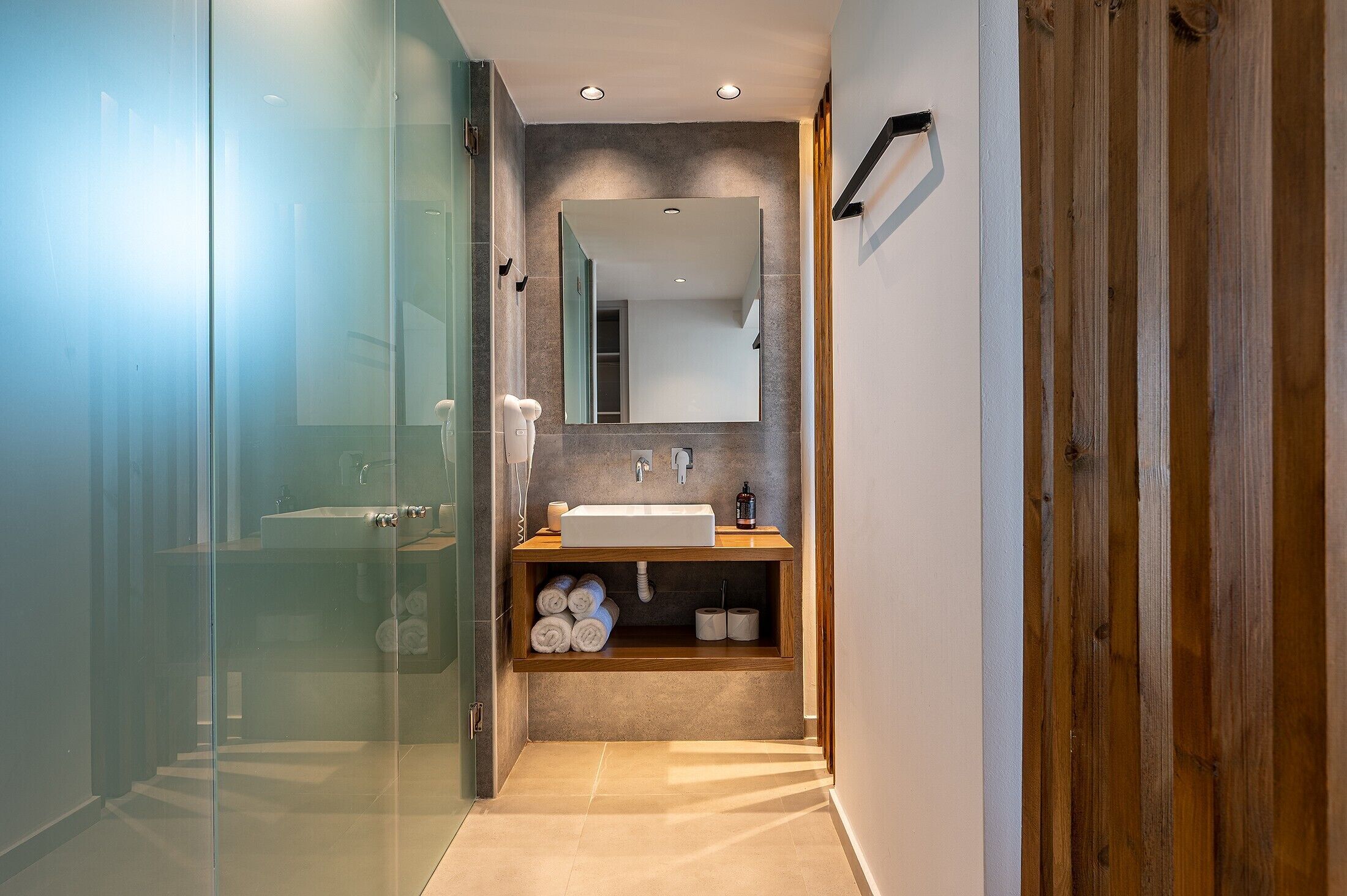 A modern bathroom with a glass shower enclosure, a sink with a wooden vanity, and a mirror above the sink.
