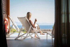 Una persona sentada en una silla reclinable blanca en un balcón con vista al agua.