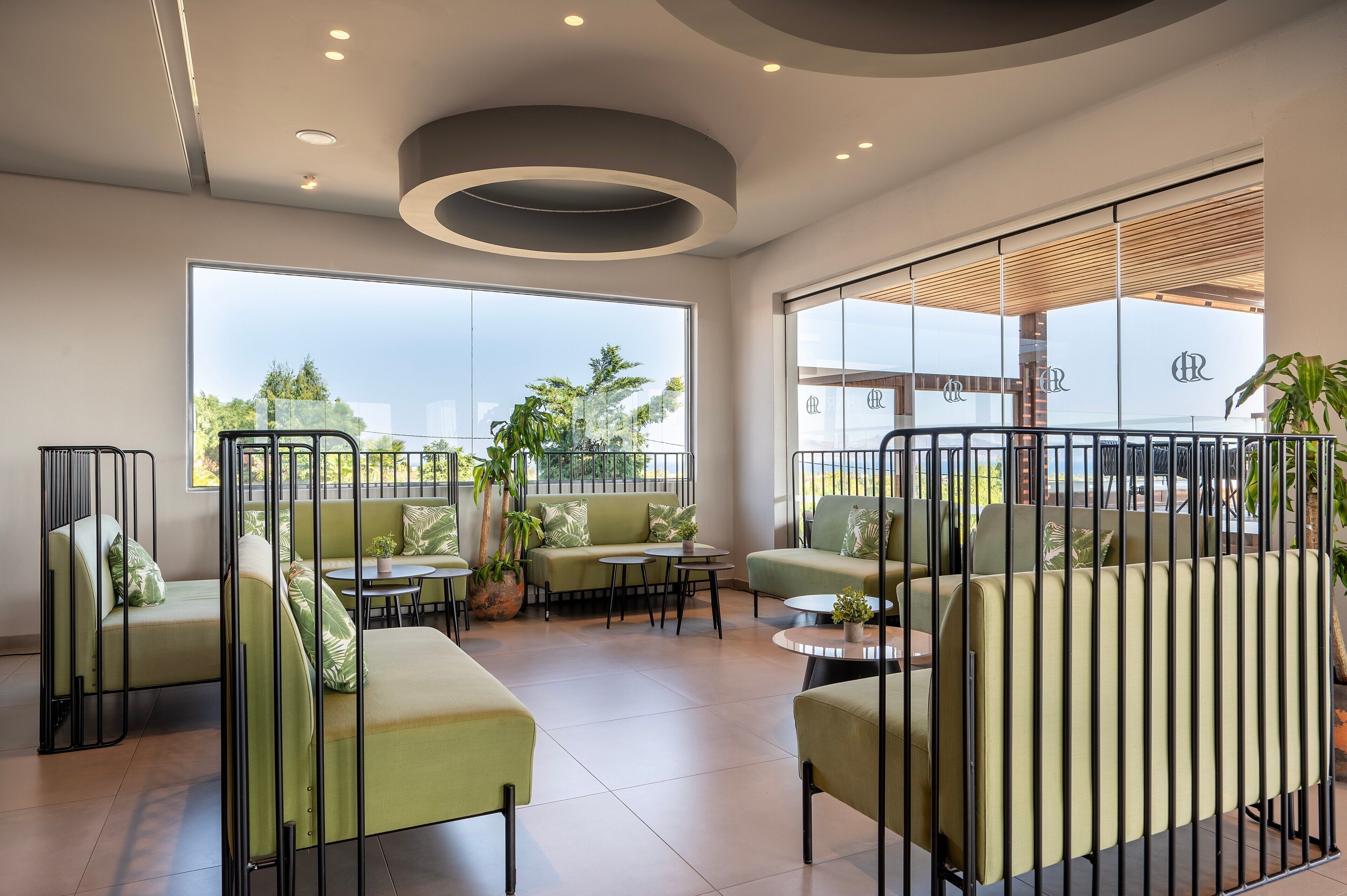 A modern lounge area with green sofas, round tables, and a view of the outdoors.