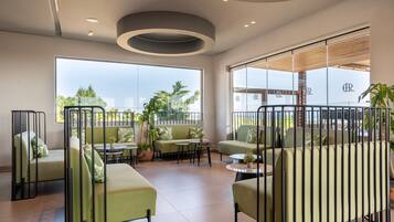 Un'area lounge moderna con divani verdi, tavoli rotondi e vista sull'esterno.