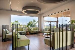 Un'area lounge moderna con divani verdi, tavoli rotondi e vista sull'esterno.