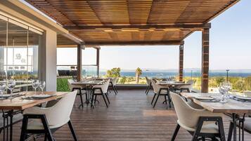 An outdoor dining area with wooden tables and chairs, overlooking a scenic landscape.