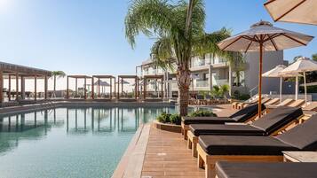A pool area with lounge chairs and umbrellas, surrounded by a wooden deck and palm trees.