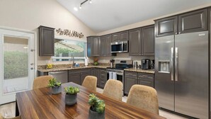 Une cuisine moderne dotée de plans de travail en granit, d’appareils électroménagers en acier inoxydable et d’un coin repas avec une table et des chaises en bois.