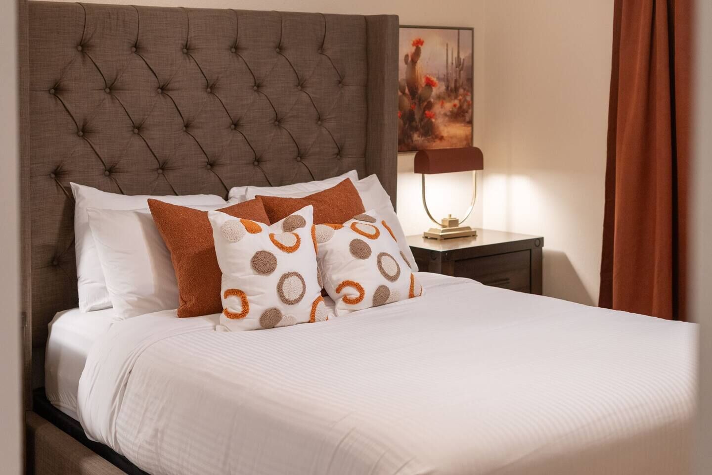 A neatly made bed with a tufted headboard, white bedding, and patterned pillows.