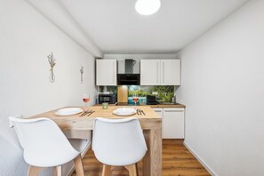 A compact kitchen with white cabinets, a wooden dining table, and two white chairs. - Ramoni Apartments - Fichtenstube - Alpirsbach (Alpirsbach)