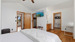 A bedroom with a bed, a ceiling fan, a TV, a desk, and a wardrobe.