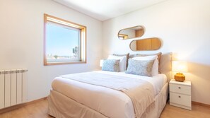 Ein Schlafzimmer mit einem großen Bett, einem Nachttisch mit Lampe, einem Fenster mit Aussicht und einem Spiegel an der Wand.