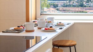 Desayuno con platos de comida, tazas y vista a una ciudad a través de una ventana.
