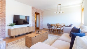 Una sala moderna con televisor de pantalla plana, muebles de madera, un comedor con sillas y una pared de ladrillo decorativa.
