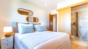 Ein Hotelzimmer mit Bett, Nachttisch, Lampe und einem Badezimmer mit Dusche und Marmorboden.