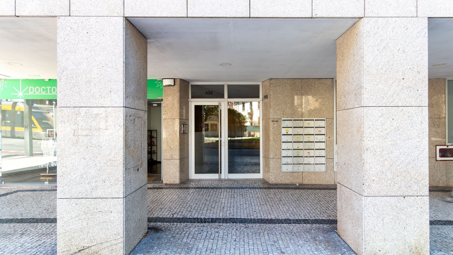 A building entrance with a glass door, a fire alarm panel, and a green sign with 'DOCTOR' on it.