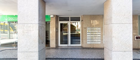 Entrada de um edifício com porta de vidro, painel de alarme de incêndio e uma placa verde com a palavra 'DOCTOR'.