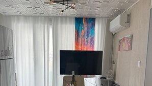 Ein modernes Wohnzimmer mit einem Marmorestisch, schwarzen Ledersesseln, einem Flachbildfernseher und einem farbenfrohen, abstrakten Gemälde an der Wand.