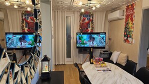 Ein Hotelzimmer mit zwei Fernsehern, einem Bett mit weißer Bettdecke, einem kleinen Tisch mit einer Flasche und Snacks sowie Weihnachtsdekorationen.