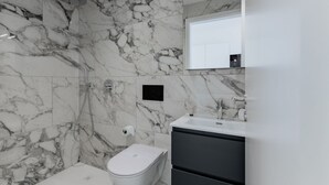 A bathroom with marble walls, a white toilet, a shower, and a sink with a mirror. - {Suite 510} Gym, Business Room, Modern, Relax (Lugano)