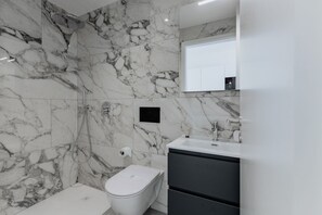 Ein Badezimmer mit Marmorwänden, einer weißen Toilette, einer Dusche und einem Waschbecken mit Spiegel.