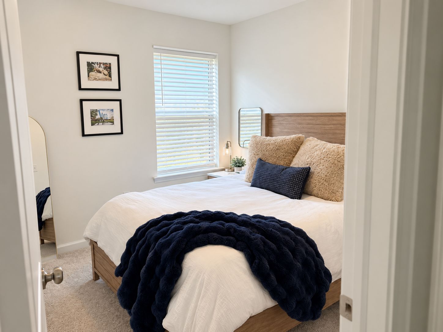 A bedroom with a bed, a window with blinds, and two framed pictures on the wall.