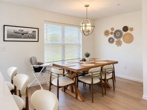 A dining area with a wooden table, six chairs, a baby stroller, and a large window with blinds. - 13 Min to Beaver Stadium | Arcade, Deck (Bellefonte)