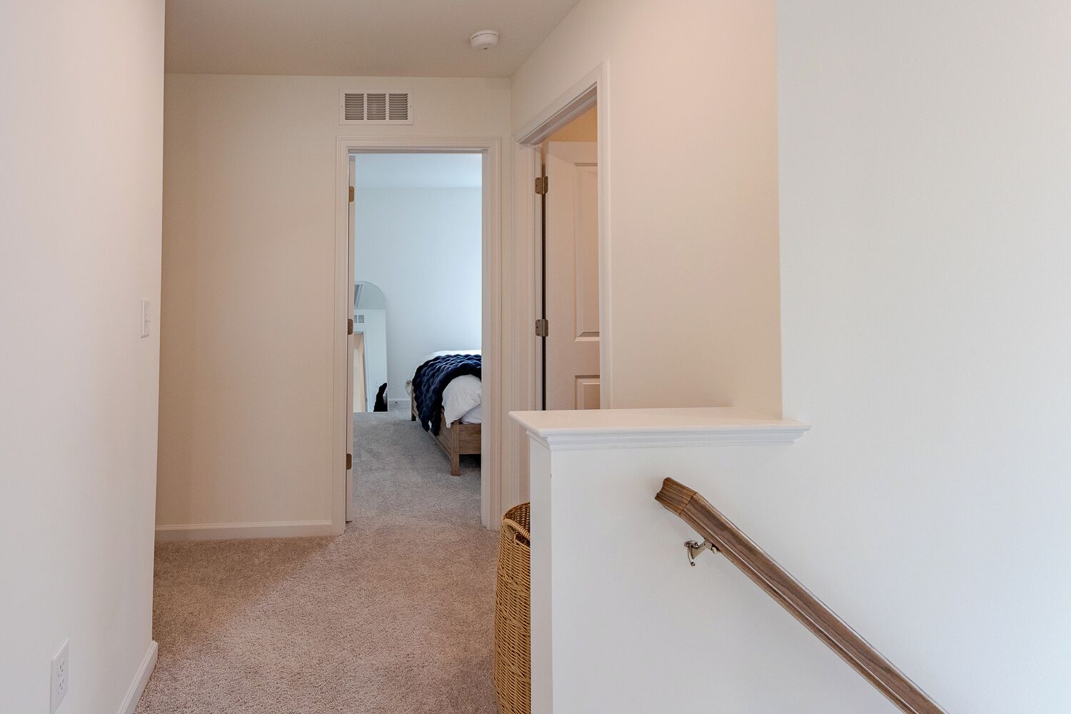 A hallway leading to a bedroom with a bed, a door, and a small basket.