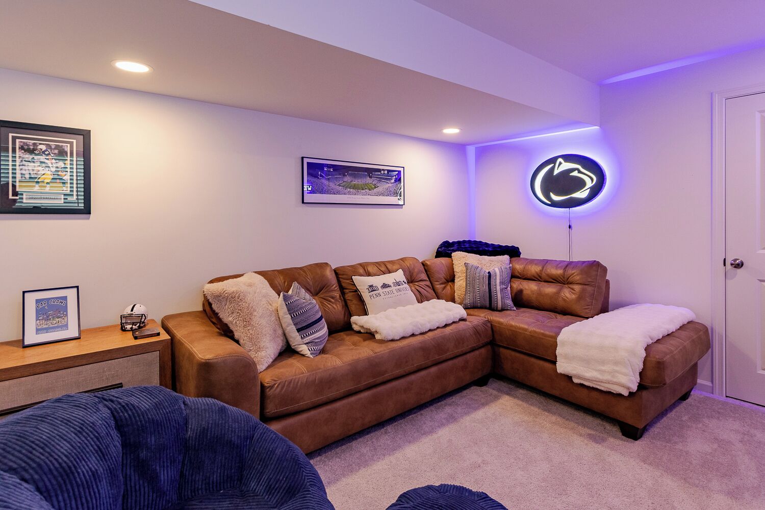 A cozy living room with a brown leather couch, a blue chair, and a framed picture on the side table.