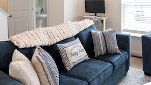 A living room with a blue sofa, a cream-colored throw blanket, and striped pillows. A framed quote is visible on one pillow. - 13 Min to Beaver Stadium | Game Room, Deck (Bellefonte)