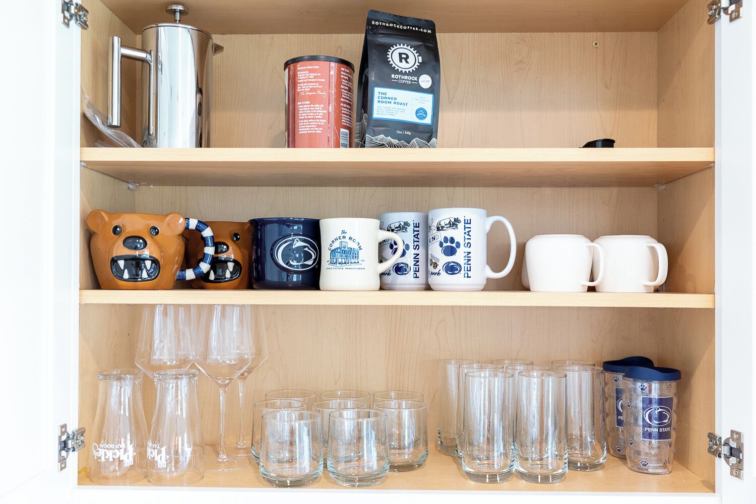 Ein Küchenschrank mit Kaffeemaschine, einer Kaffeedose und Tassen mit Penn State Logo.