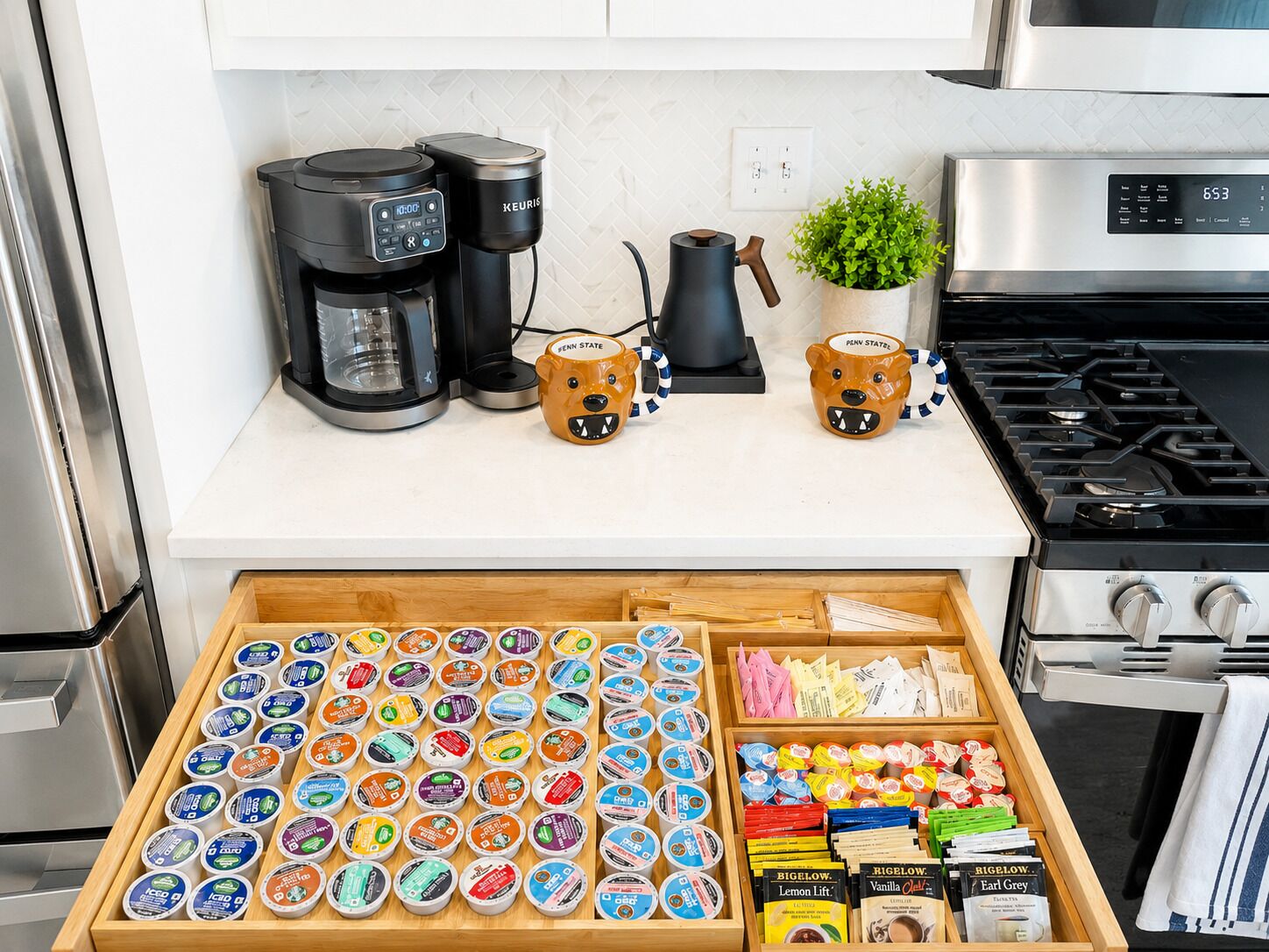 A kitchen counter with a coffee maker, mugs, and a drawer of food items.