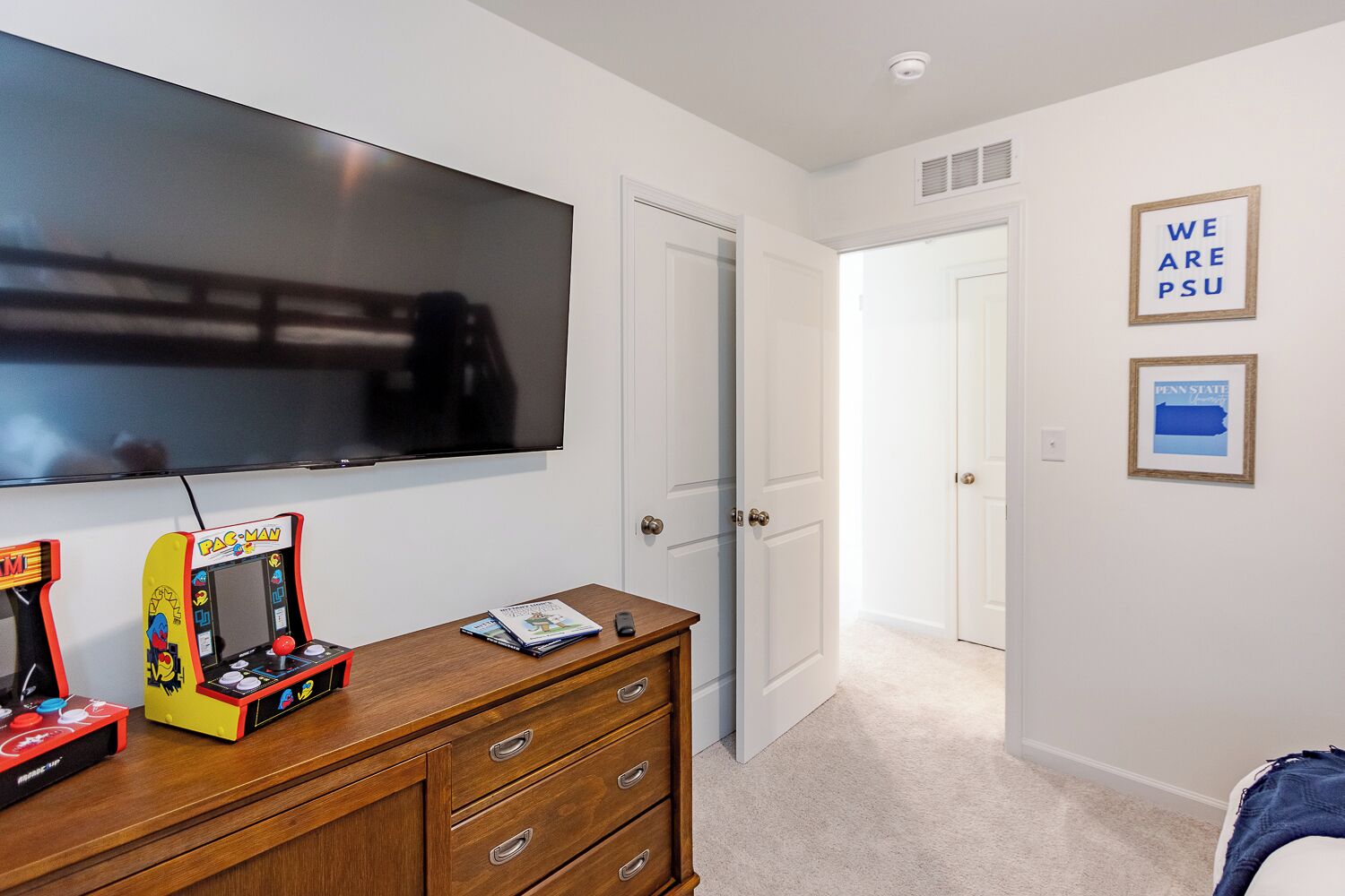 A room with a television, Pac-Man arcade games, a wooden dresser, and a door leading to another room.