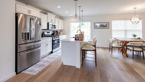 A modern kitchen with stainless steel appliances, a central island, and a dining area with a wooden table and chairs. - 13 Min to Beaver Stadium | Game Room, Deck (Bellefonte)