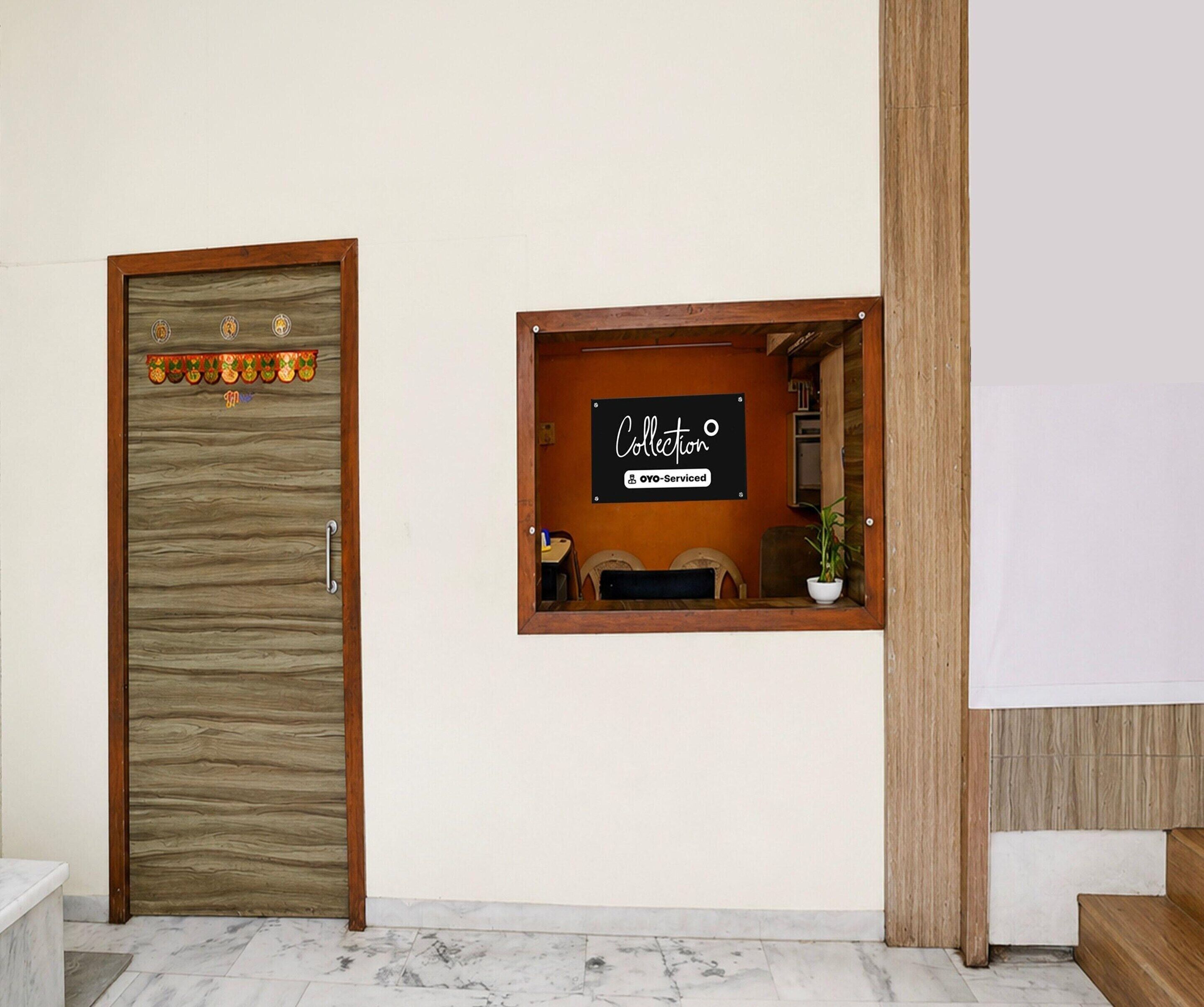 A reception area with a wooden door, a sign indicating 'Collection' and 'OYO-Serviced', and a small window with a desk and chair.