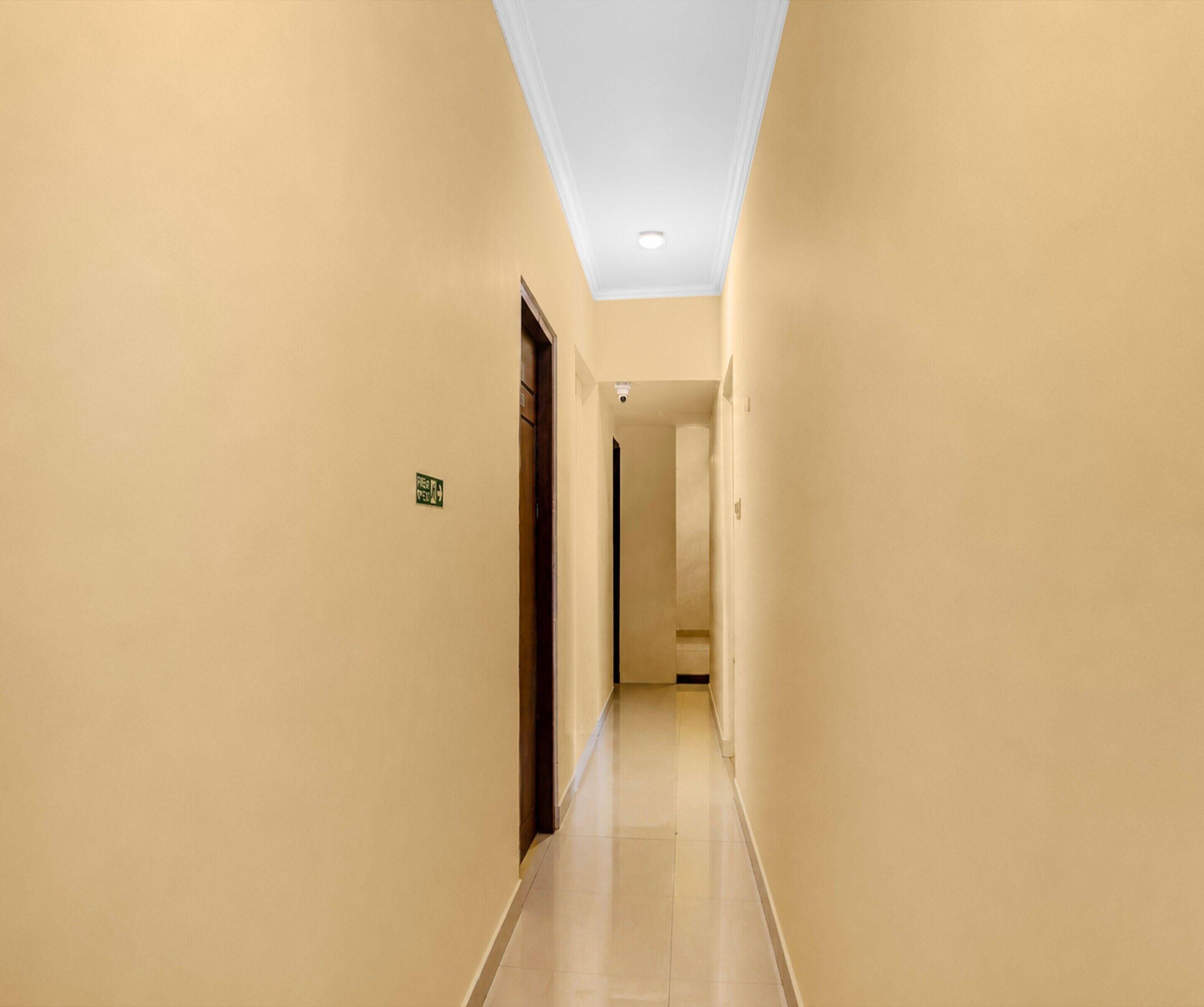 A narrow, well-lit hallway with beige walls and a tiled floor, leading to a door at the end.