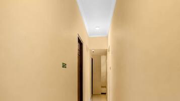 A narrow, well-lit hallway with beige walls and a tiled floor, leading to a door at the end.
