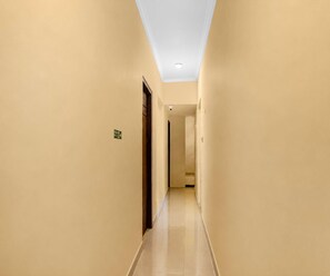 Un pasillo estrecho y bien iluminado con paredes color beige y piso de baldosas, que conduce a una puerta al final.