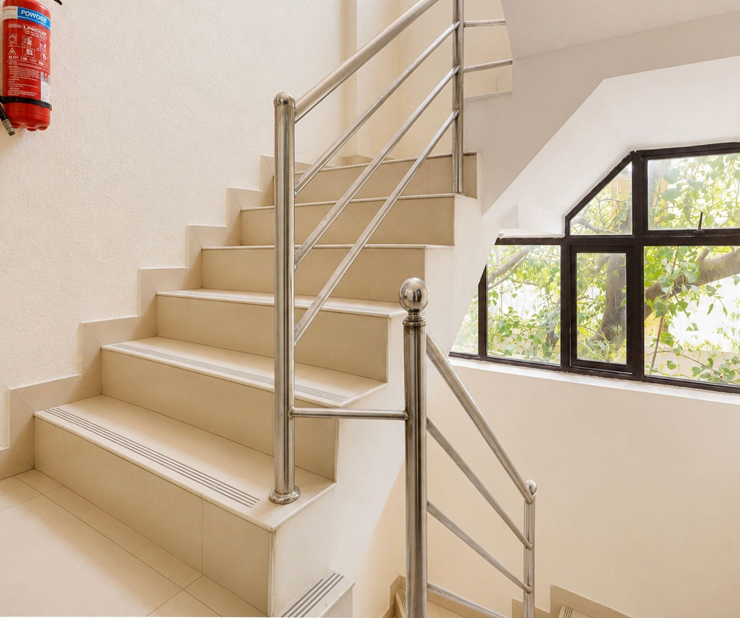 A staircase with a metal handrail and beige steps, leading to a room with a window overlooking greenery.