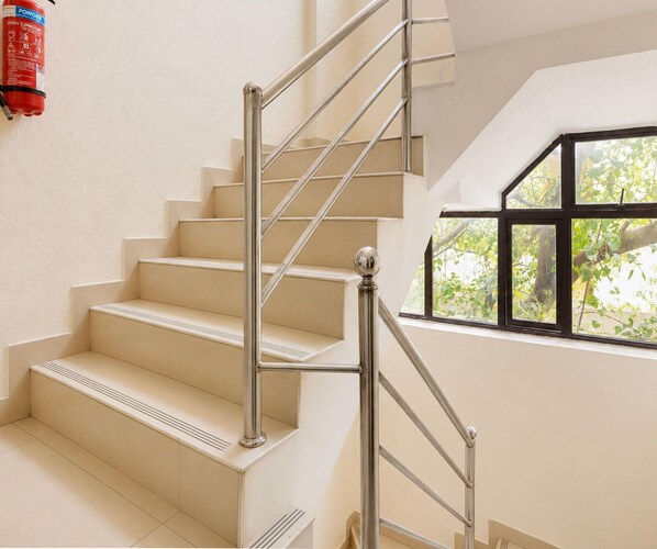 A staircase with a metal handrail and beige steps, leading to a room with a window overlooking greenery.