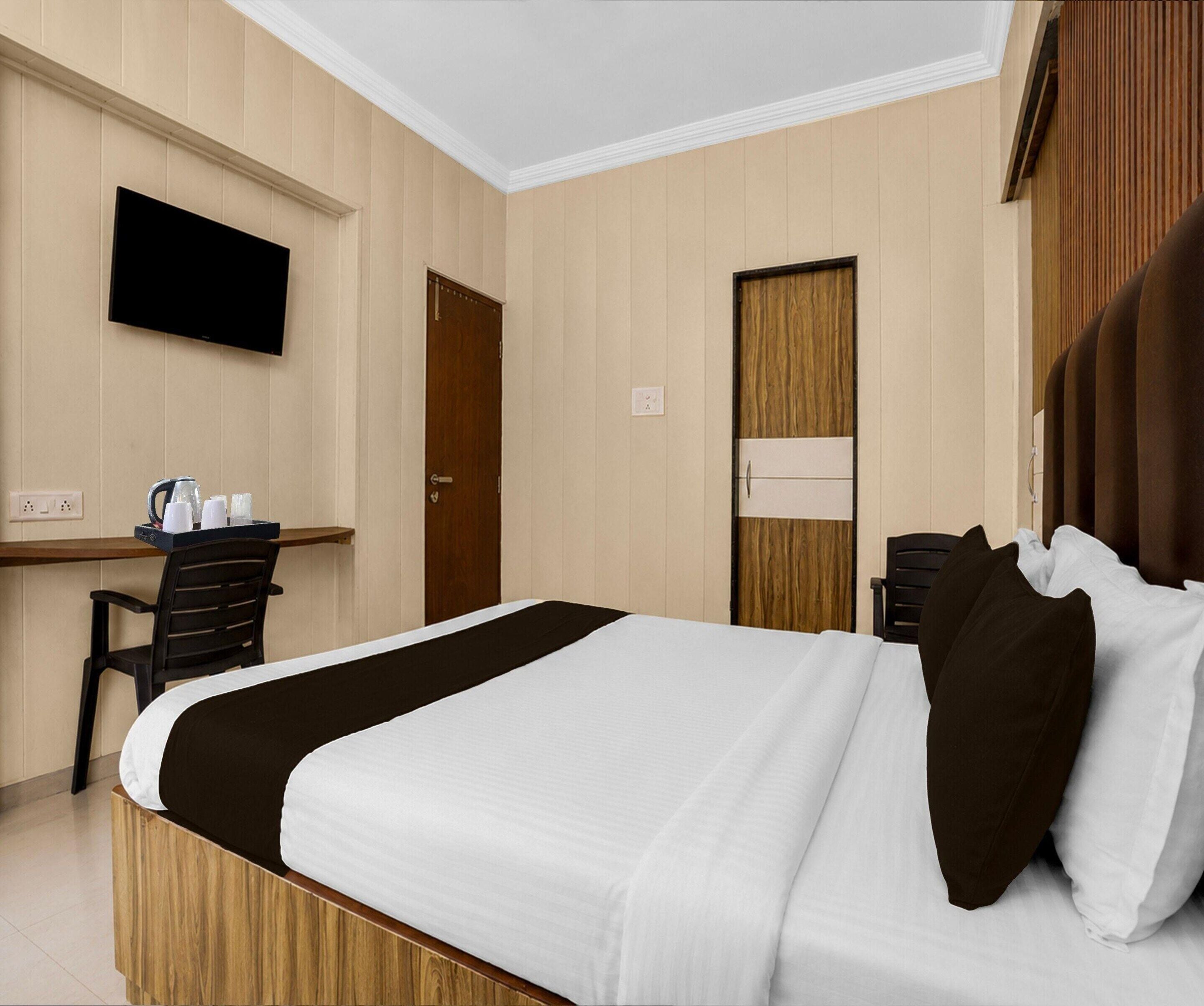 A hotel room with a bed, a desk, a chair, a television, and a wardrobe.