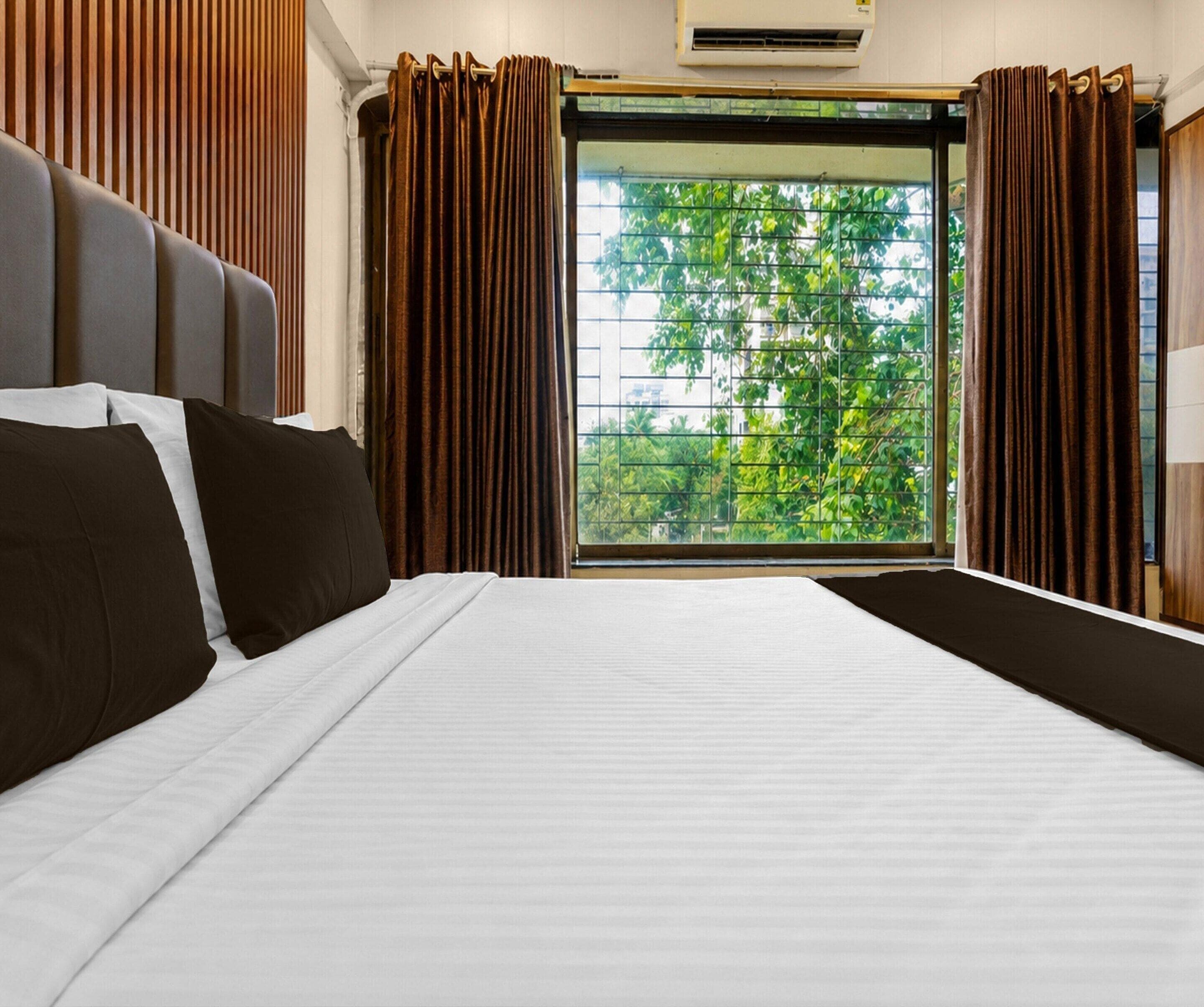 A hotel room with a bed, curtains, and a window with a view of trees.