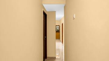 A corridor with beige walls and a tiled floor, leading to a room with a door and a window with a flower decoration.