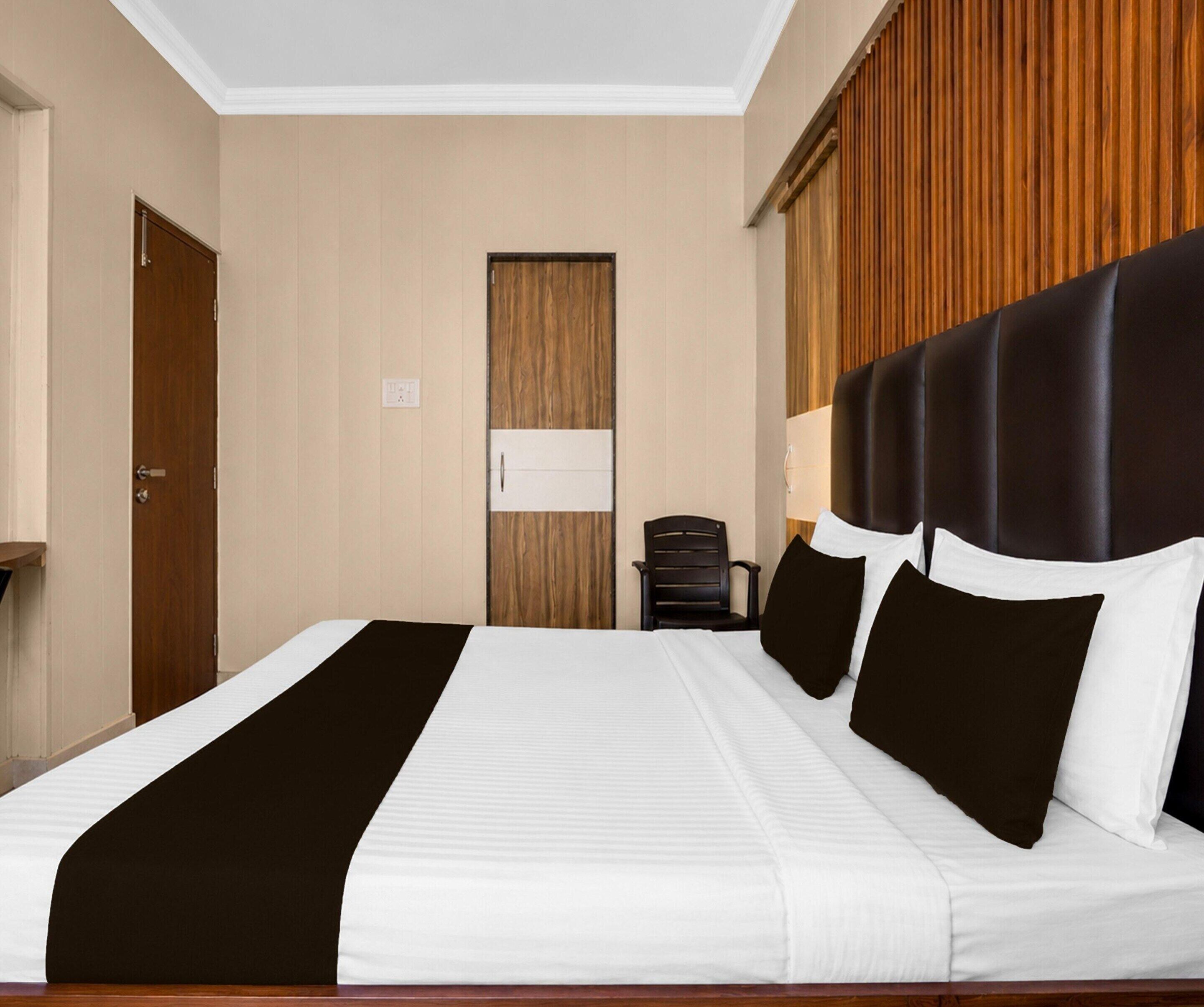 A hotel room with a large bed, a wooden door, a wall-mounted light, and a wooden panel wall.