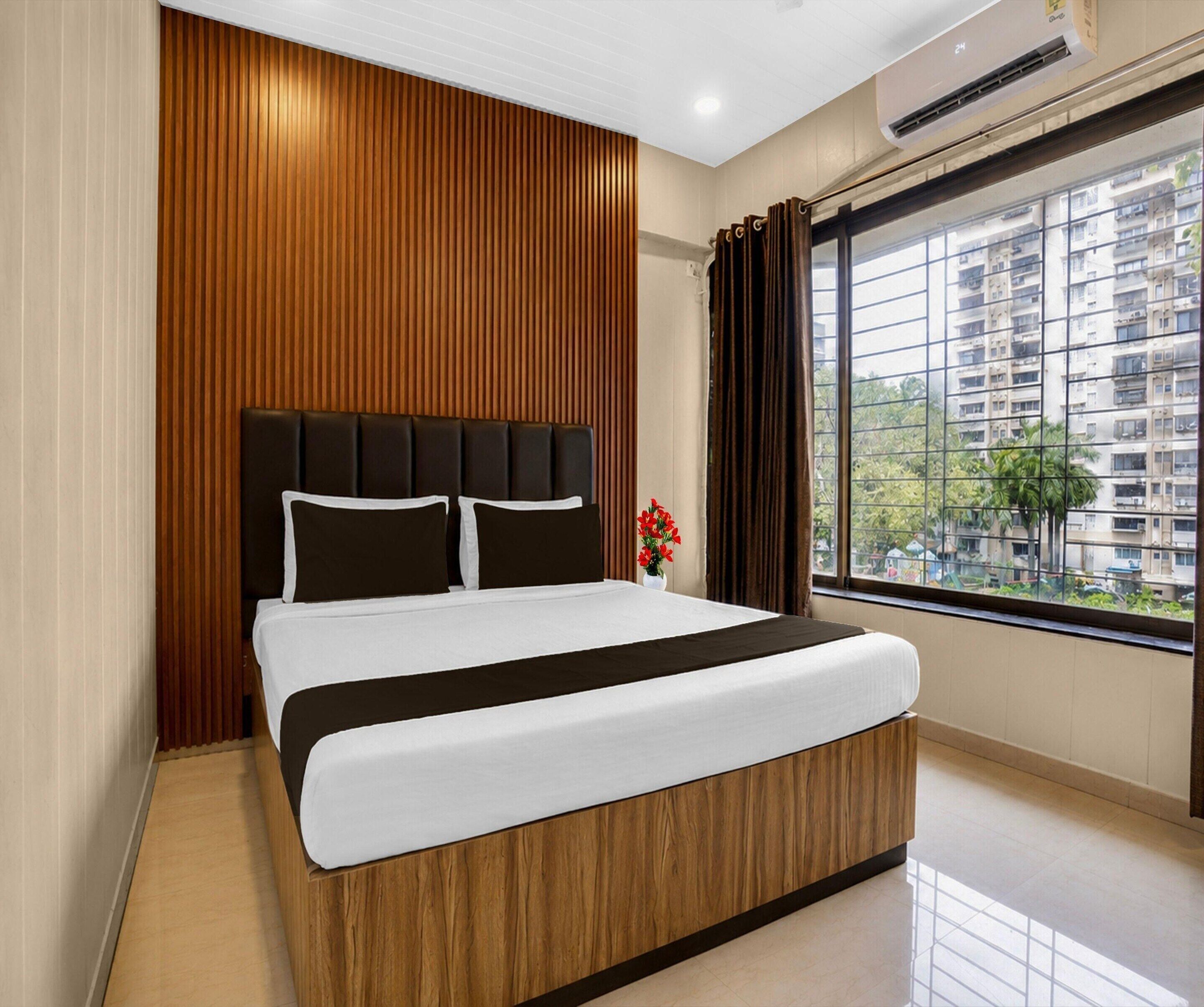 Habitación de hotel moderna con una cama grande, paneles de madera, un ventanal con vistas a la ciudad y un equipo de aire acondicionado.
